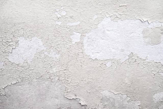 A white wall with peeling paint on it.